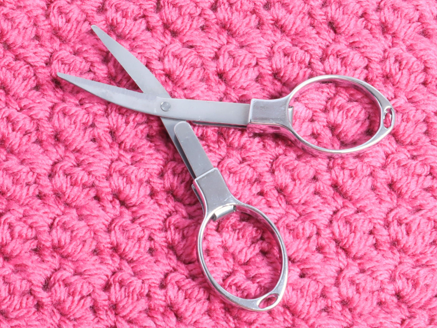 Folding scissors unfolded on a pink background