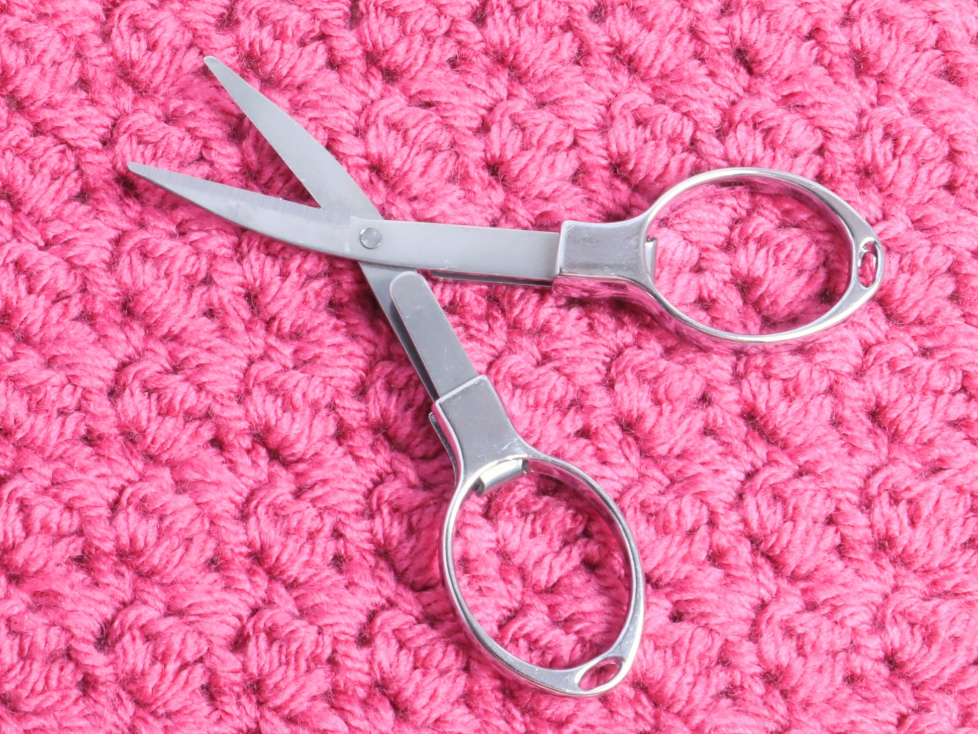 Folding scissors unfolded on a pink background
