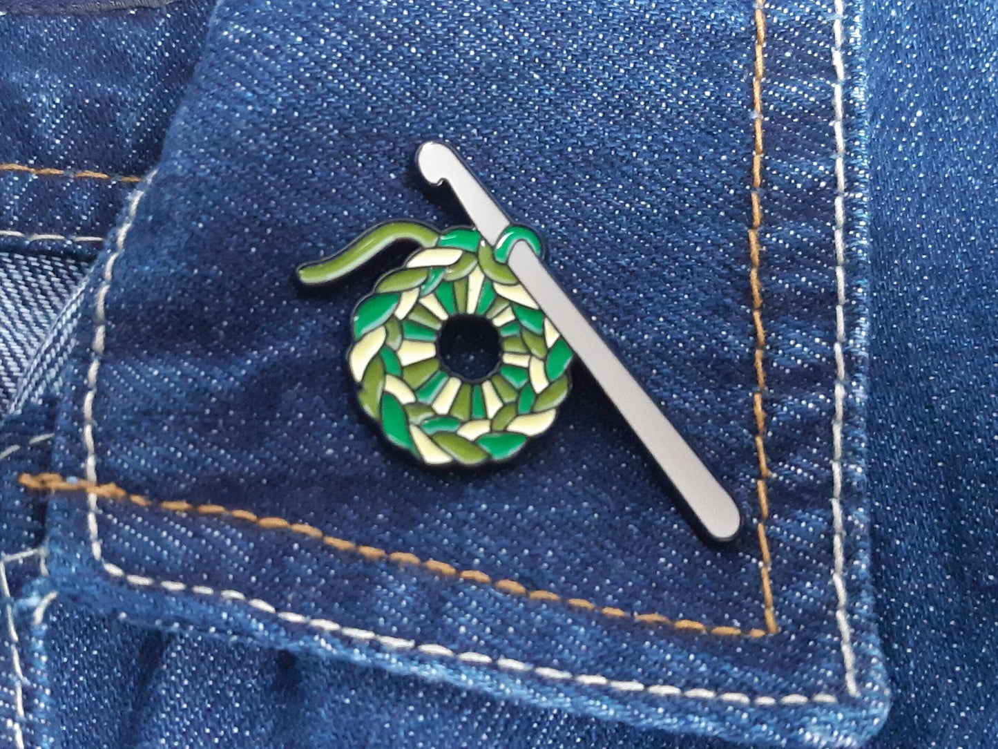 green crocheted ring with crochet hook pin badge on a denim jacket collar